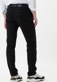 Pantaloni neri con una vestibilità slim, dotati di due tasche posteriori e una trama liscia. Indossati con una cintura nera e scarpe da ginnastica beige.
