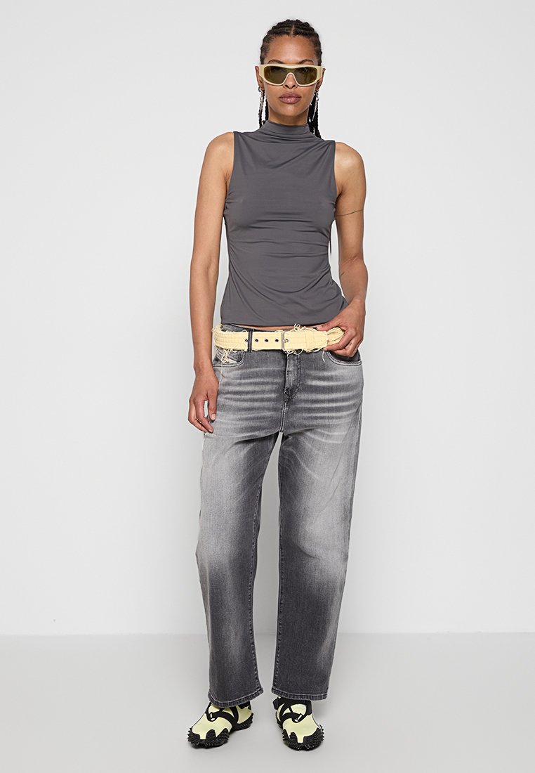 Top grigio senza maniche con collo alto; cintura giallo chiaro; jeans grigi strappati; calzature nere e gialle; occhiali da sole con montatura traslucida.