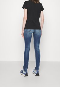 Camiseta negra de manga corta combinada con pantalones vaqueros ajustados de color azul. Los pantalones cuentan con un diseño clásico de cinco bolsillos y costuras visibles.