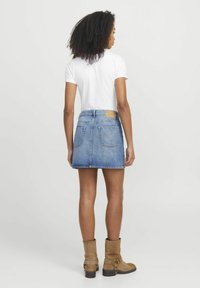 Jeanskjørt med lys blå vask, med to baklommer og en etikett på livet, kombinert med en hvit T-skjorte og brune ankelstøvletter.