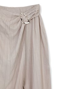 Pantaloni beige a pieghe con dettaglio in vita torsionata, realizzati in un tessuto texturizzato e con accenti in metallo. Superficie liscia con linee sottili.
