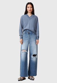 Lichtblauwe gebreide v-hals trui; wijd gesneden distressed denim jeans met rafelrand; zwarte gestippelde ballerina's. Eenvoudig en modern ontwerp.