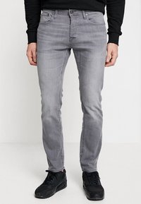 Grå denimjeans med slim fit, fem fickor och knappstängning. I kombination med svarta sneakers och en långärmad svart skjorta.