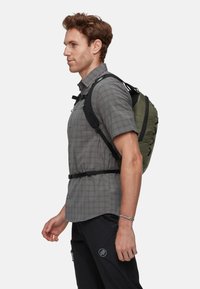 Grau karierter Kurzarmhemd, schwarzer Rucksack mit grünen Akzenten, getragen von einem Mann. Verstellbare Träger und Schnurschluss sichtbar.