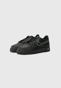 Sapatilhas pretas de pele com uma caixa de dedos perfurada, atacadores e uma sola de borracha. Destaca-se o logótipo prateado da Nike e o texto "AIR" no calcanhar.