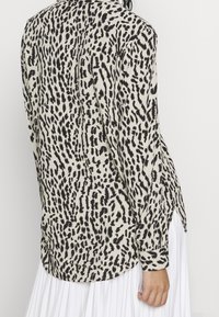Mujer vestida con una blusa de leopardo en blanco y negro de manga larga, combinada con una falda blanca plisada, vista desde atrás.
