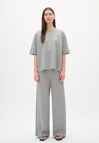 Set di abbigliamento loungewear grigio composto da una maglietta a maniche corte e una vestibilità ampia, insieme a pantaloni a gamba larga, realizzati in un tessuto morbido con una texture liscia.