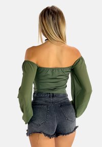 Top verde oliva off-the-shoulder con maniche a sbuffo, abbinato a pantaloncini di jeans neri a vita alta con orli sfrangiati e tasche posteriori.