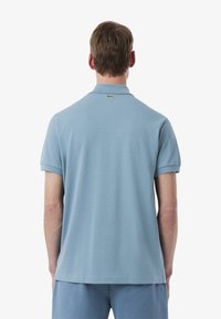 Jasnoniebieska koszulka polo z krótkim rękawem, wykonana z teksturowanej bawełny, z kołnierzykiem. Posiada małe zielone logo na tylnej części kołnierza.