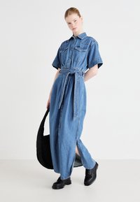 Denim kreklis ar īsām piedurknēm, ar pogājamu priekšu, piesieta josta, gara garuma, sānu šķēlumi un kontrastējoša melna josta, stilizēts ar melniem apaviem.