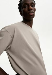 Tricou oversized de culoare bej deschis, cu guler rotund și mâneci scurte, realizat dintr-un material moale cu o textură netedă.