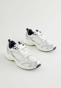 Scarpe da ginnastica bianche e argento con tomaia in rete, colletto imbottito e suola in gomma. Presentano lacci bianchi e dettagli blu navy.