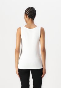 White sleeveless tank top with a round neckline, made of soft fabric, smooth texture, and a fitted design, paired with black pants.