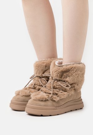 Tan värfodrade ankelstövlar med texturerad fuskpälsövre del, snörning fram, och tjock gummisula, med rund tå och mjukt inre.