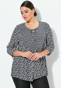 Blusa floreale bianca e nera con scollatura rotonda, dettaglio con bottoni a chiave e maniche a trequartini, realizzata in tessuto leggero.