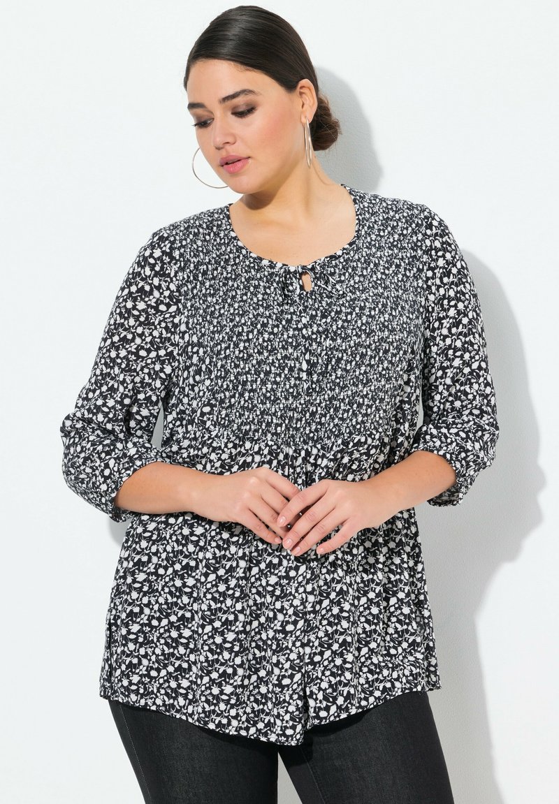 Blusa floreale bianca e nera con scollatura rotonda, dettaglio con bottoni a chiave e maniche a trequartini, realizzata in tessuto leggero.