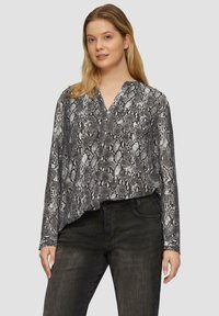 Lange mouw blouse in zwart-witte slangenprint, met een v-hals en zachte stof. Gecombineerd met donkere spijkerbroeken, die een relaxte pasvorm laten zien.