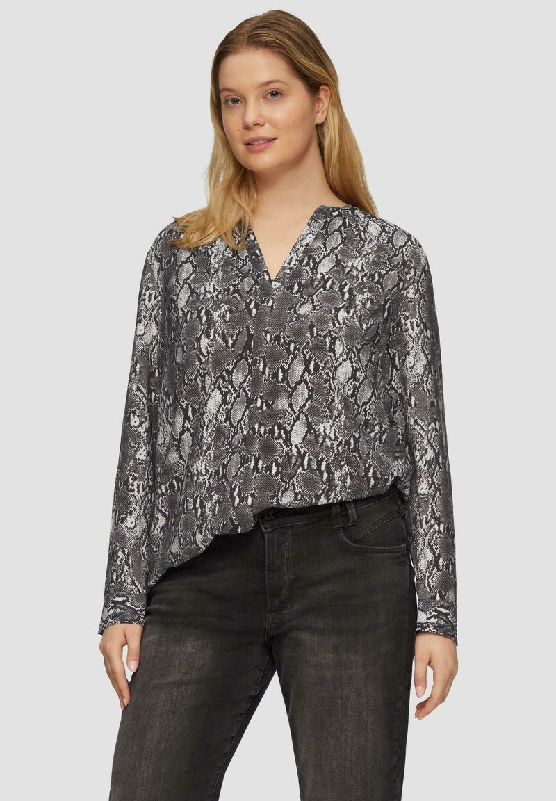 Lange mouw blouse in zwart-witte slangenprint, met een v-hals en zachte stof. Gecombineerd met donkere spijkerbroeken, die een relaxte pasvorm laten zien.