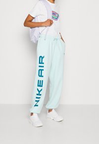 Světle modré tepláky s tučným tmavě modrým nápisem "NIKE AIR" na levé nohavici, kombinované s bílým tričkem a bíl ými sneakers.