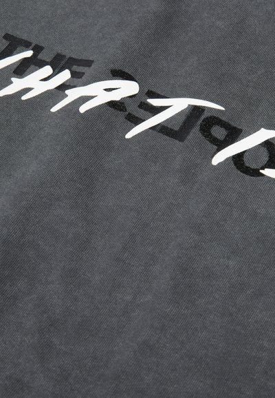 Un tissu gris présentant un design de texte stylisé en blanc audacieux. La texture est lisse avec un léger éclat. Le texte a un aspect graphique en couches.