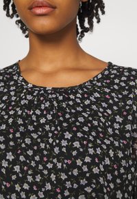 Blusa preta com padrão floral, apresentando um decote redondo, tecido leve e um delicado padrão de pequenas flores brancas e rosas.