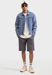 Denimjakke, hvid t-shirt, grå shorts, beige sneakers, sort/hvide stribede sokker og solbriller. Casual outfit med kontrasterende teksturer.