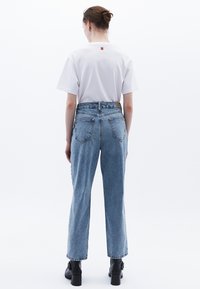 Valkoinen lyhythihainen t-paita, jossa on pieni logo selässä, yhdistettynä vaaleansinisiin korkeavyötäröisiin suoriin farkkuihin ja mustiin paksupohjaisiin saappaisiin.