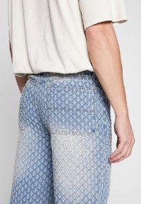 Ljusblå denimjeans med en strukturerad mönster och urtvättning, med två bakfickor och en avslappnad passform. Justerbar midjeband är synlig.