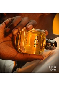 Firkantet glassparfymeflaske med en mørk metallkapsel, fylt med ravfarget væske. Etiketten leser "Emporio Armani Stronger With You" i svart.