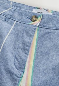 Short bleu avec des rayures verticales pastel près du bouton et une boucle de ceinture visible, avec un bouton marron marbré et une étiquette blanche indiquant NEXT.