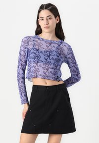 Feszes, áttetsző lila cropped top virágmintával; hosszú ujjú. Magas derekú fekete szoknyával párosítva, kapcsos részletekkel és zsebekkel.