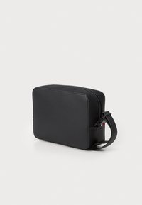Black rectangular bag made of smooth leather with a zip closure, short strap, and minimalistic design. Notable red accent on the side.
