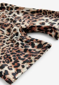 Chemise imprimée léopard avec un tissu lisse et léger, à manches retroussées, dans des tons de marron et noir sur un fond beige.