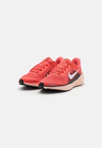 Crvene mrežaste atletske tenisice imaju elegantan dizajn, s bijelim swoosh logom, crnim detaljima i udobnom bež potplatom. Čipke su istaknute.
