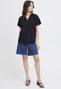 Haut noir à manches courtes avec un col en V et un col volanté, associé à un short en denim bleu jusqu'aux genoux et des sandales à talons carrés noires.