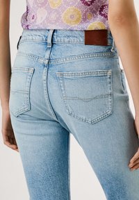 Gai zili džinsi ar izbalējušu apdari. Iespējotas divas aizmugures kabatas un brūns ādas uzlīme jostasvietā.