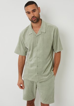 Camisa de mangas cortas verde claro y pantalones cortos a juego, fabricados en un tejido suave y texturizado, con un corte relajado y detalles de botones en la camisa.
