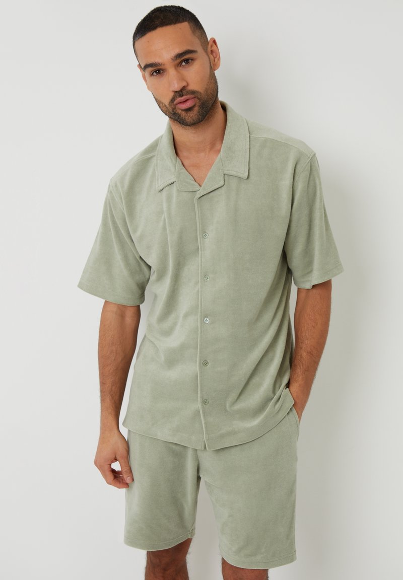 Chemise à manches courtes vert clair et short assorti en tissu doux et texturé avec une coupe décontractée et des détails de boutons sur la chemise.
