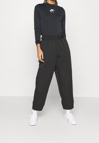 Svart ribbad långärmad tröja med vit Nike-logga, kombinerad med löst sittande svarta byxor med elastisk midja och fickor. Vita sneakers.