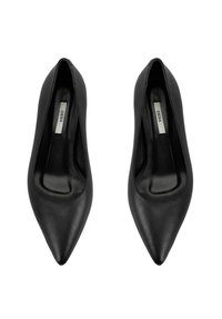 Escarpins en cuir noir à bout pointu avec une texture lisse, présentant une ouverture incurvée et une semelle intérieure rembourrée. Marque visible à l'intérieur.