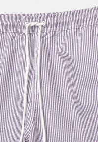 Lila és fehér csíkos fürdőnadrág, elasztikus derékkal és húzózsinórral. Könnyű anyagból készült, texturált felülettel.