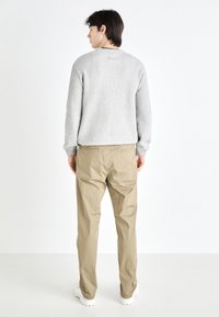 Suéter gris de canalé con cuello redondo, combinado con pantalones beige. La modelo es vista de espaldas, mostrando un ajuste relajado.