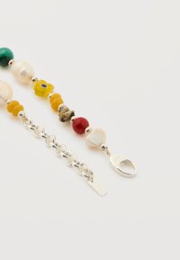 Ασημένιο βραχιόλι αλυσίδα με μικτά χάντρες, συμπεριλαμβανομένων μαργαριταριού, κίτρινο λουλούδι, κόκκινες και πράσινες χάντρες σε λευκό φόντο.