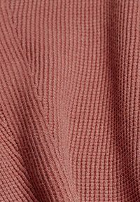Tissu texturé dans une teinte de rose muted, présentant un motif en côtes avec des lignes en relief, doux au toucher et légèrement réfléchissant.