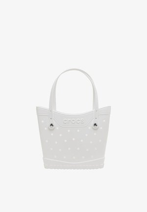 Witte Crocs draagtas met verstelbare handvatten en ronde gaten in een polkadotpatroon op het lichaam.