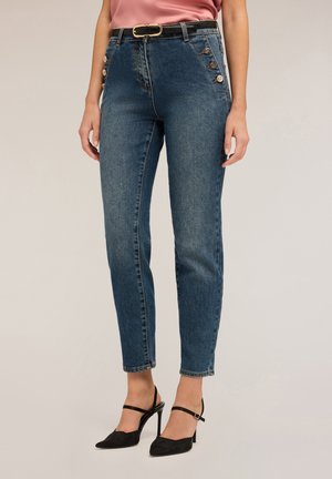 Hoge taille blauwe jeans met zijknopdetails en een slanke pasvorm. Gecombineerd met zwarte slingback hakken en een lichtroze top.