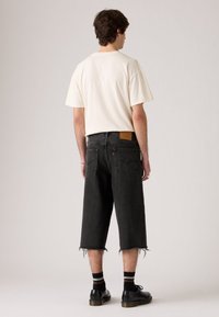 Sorte denimshorts med frynser i kanten, parret med en kortærmet cremefarvet T-shirt og sorte snørebåndssko, der har stribede strømper.
