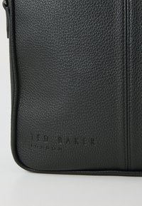 Zwarte leren tas met textuur, featuring een gladde afwerking, reliëflogo "TED BAKER LONDON" en ritsluiting langs de bovenrand.