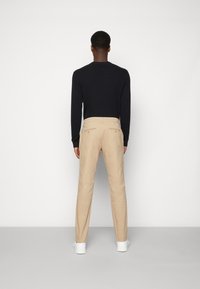 Beige trousers made of cotton, slim fit, featuring back pockets with buttons, worn with a black sweater and white sneakers.