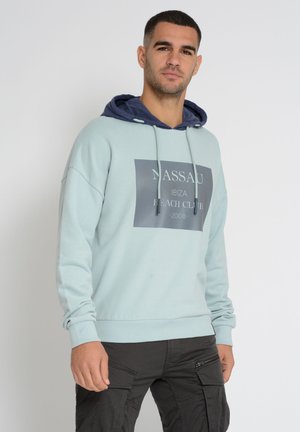 Light blue sweatshirt with navy hoodie, featuring a large graphic print stating "NASSAU IBIZA BEACH CLUB 2008," and drawstring accents.
